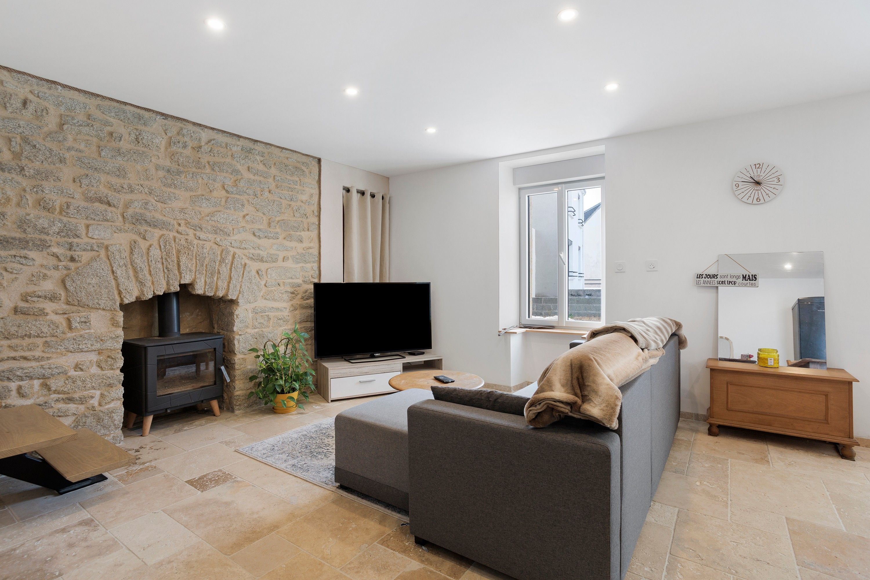 A living room with a stone wall, a television, a sofa, a small table, and a window.