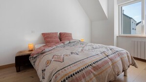 A bedroom with a sloped ceiling, a large window, a bed with patterned bedding, and two bedside lamps.