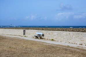 Une vue sur la côte, avec un mur de pierre, un banc et un phare au loin.