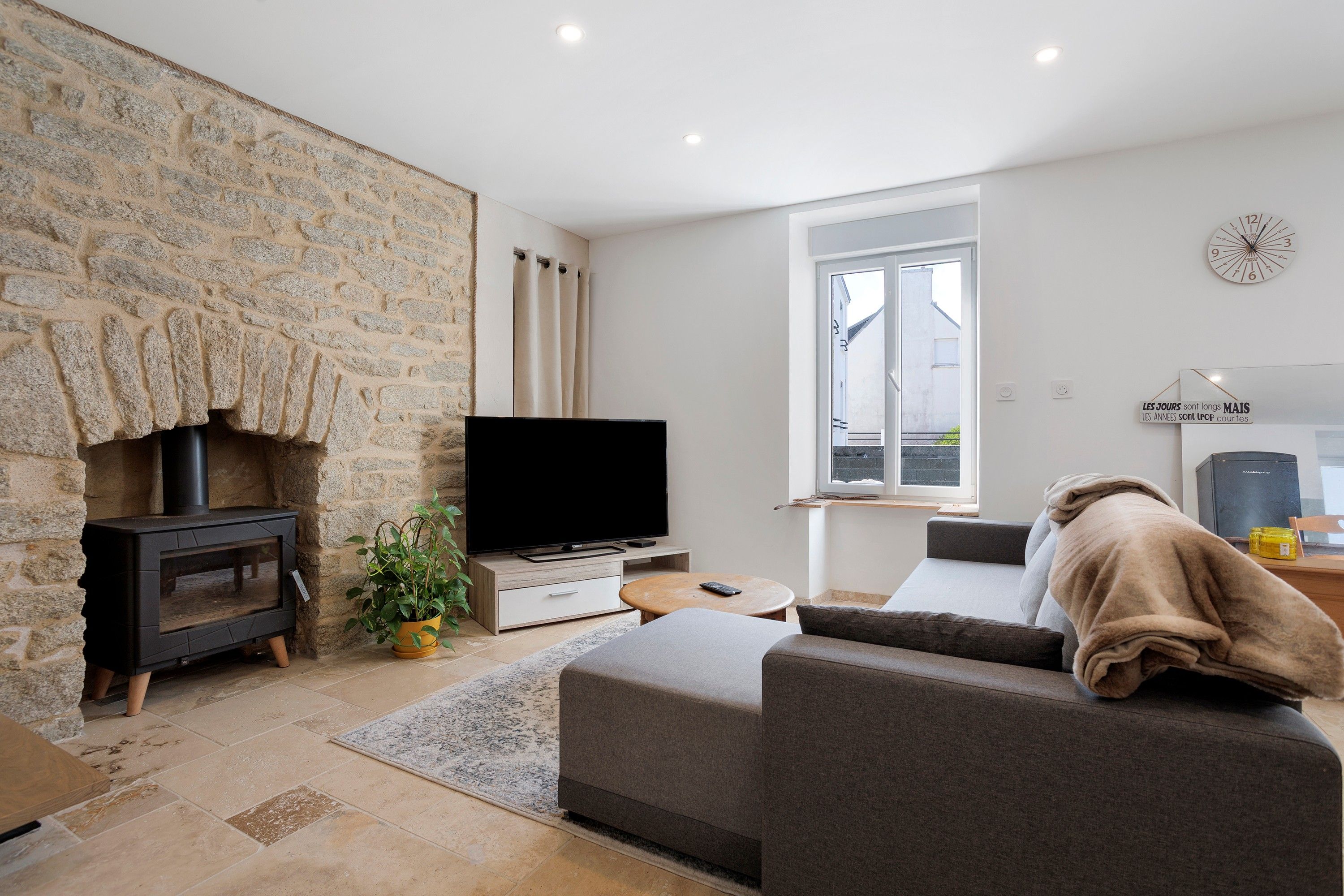 A modern living room with a stone wall, a fireplace, a flat-screen TV, a sofa, and a window.