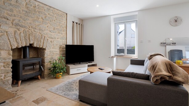 A modern living room with a stone wall, a fireplace, a flat-screen TV, a sofa, and a window.