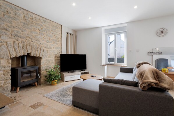 A modern living room with a stone wall, a fireplace, a flat-screen TV, a sofa, and a window.