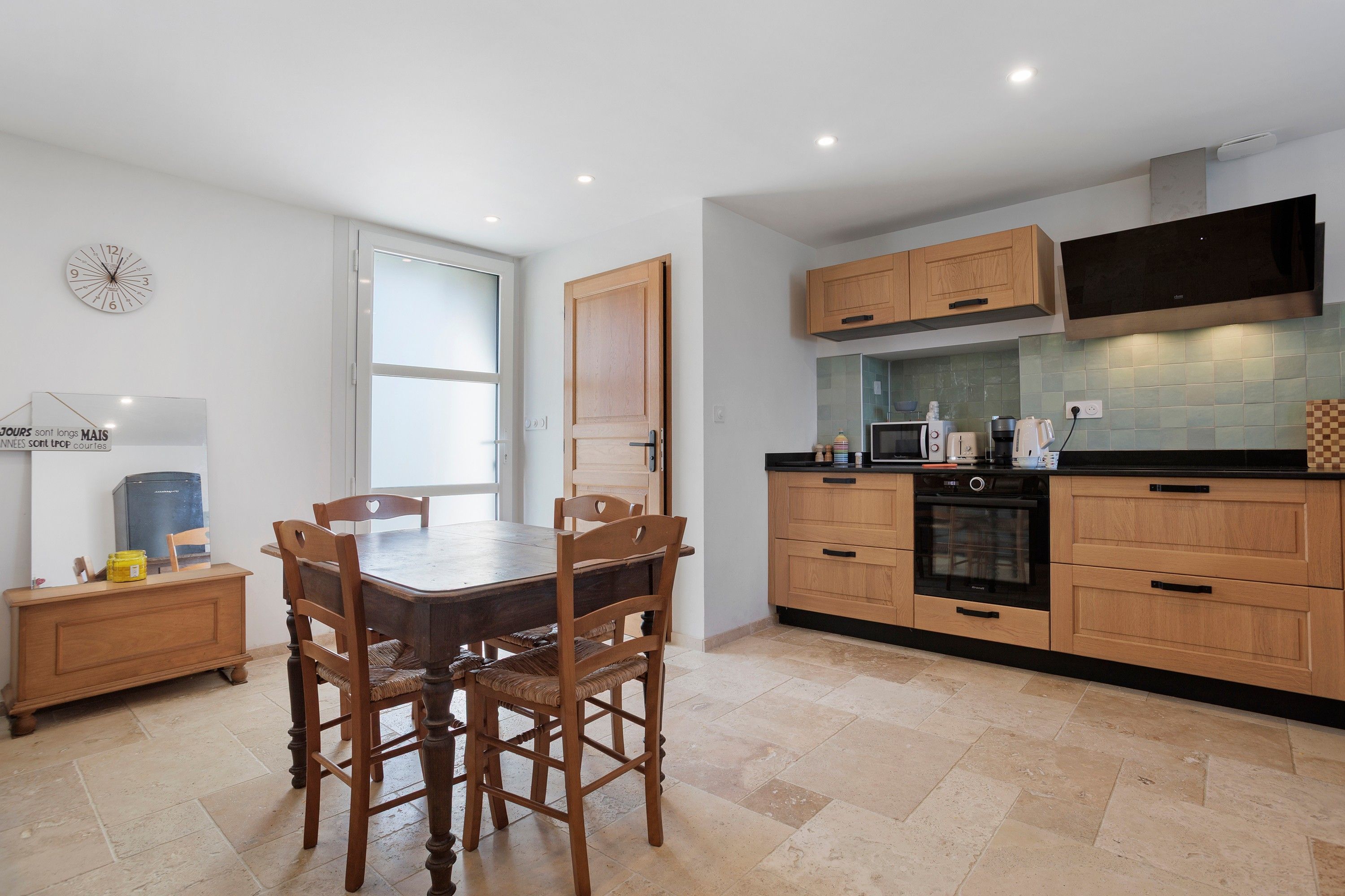 A modern kitchen with wooden cabinets, a built-in oven, and a dining area with a table and chairs.