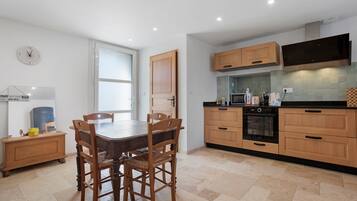 A modern kitchen with wooden cabinets, a built-in oven, and a dining area with a table and chairs.
