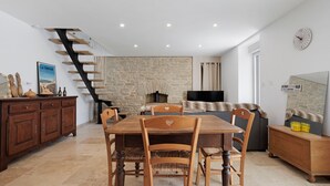 A dining area with a wooden table and chairs, a stone wall, a fireplace, and a staircase.