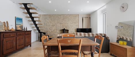 Un comedor con una mesa y sillas de madera, una pared de piedra, una chimenea y una escalera.