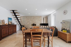 A dining area with a wooden table and chairs, a stone wall, a fireplace, and a staircase.