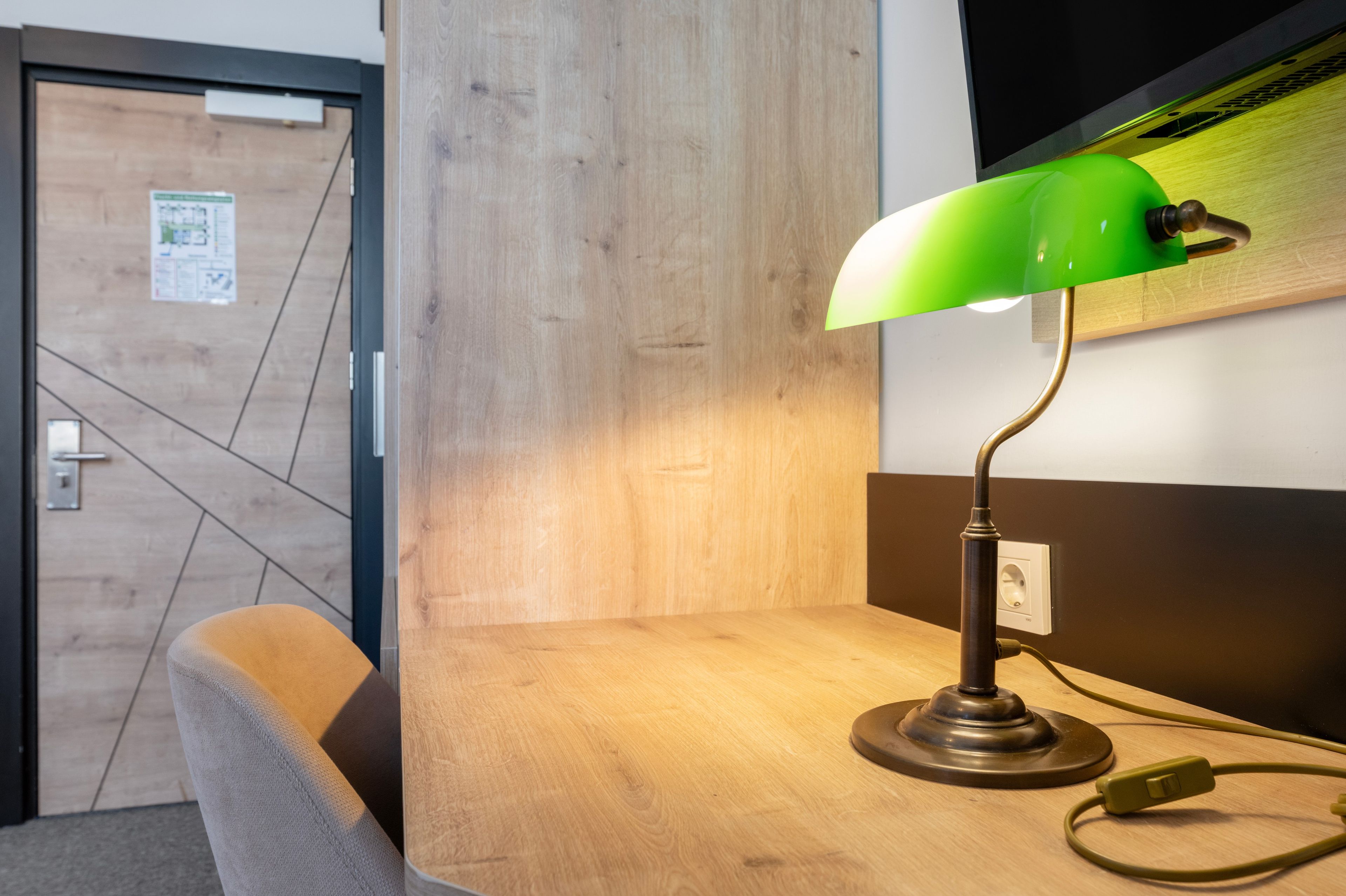 Ein Holztisch mit einer grünen Schreibtischlampe, einem Stuhl und einer Wandsteckdose.