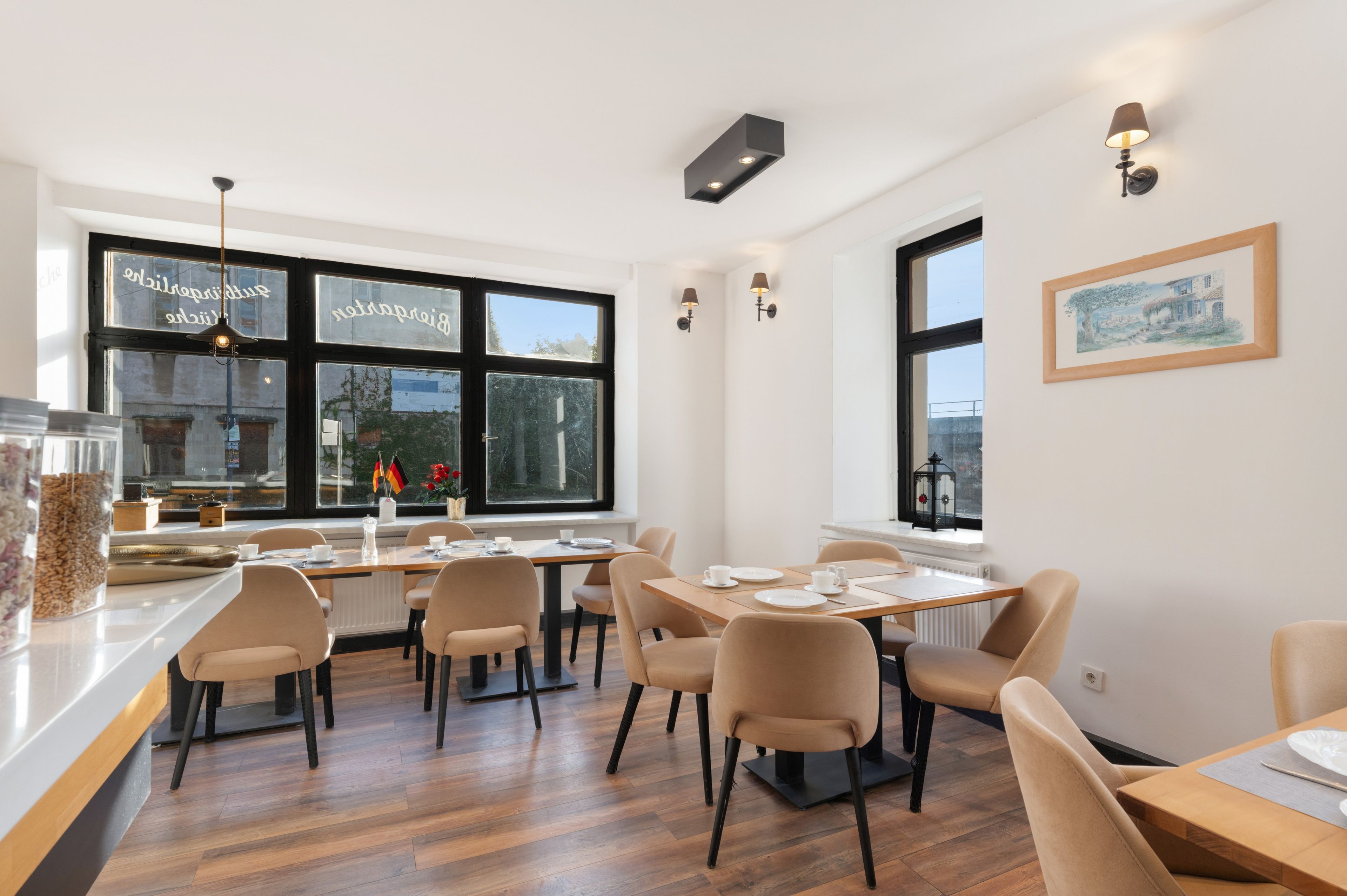 A dining area with tables set for four, chairs, a window with a view, and a wall-mounted light fixture.