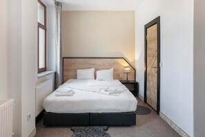 A neatly made bed with white linens and towels, a bedside lamp, and a wooden headboard.
