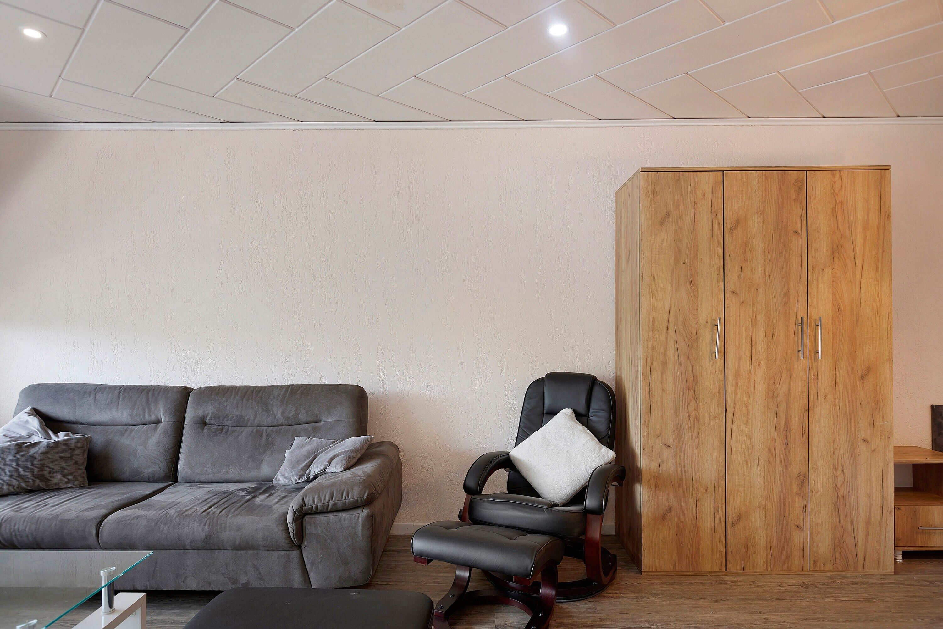 A living room with a grey sofa, a black leather chair, and a wooden wardrobe.