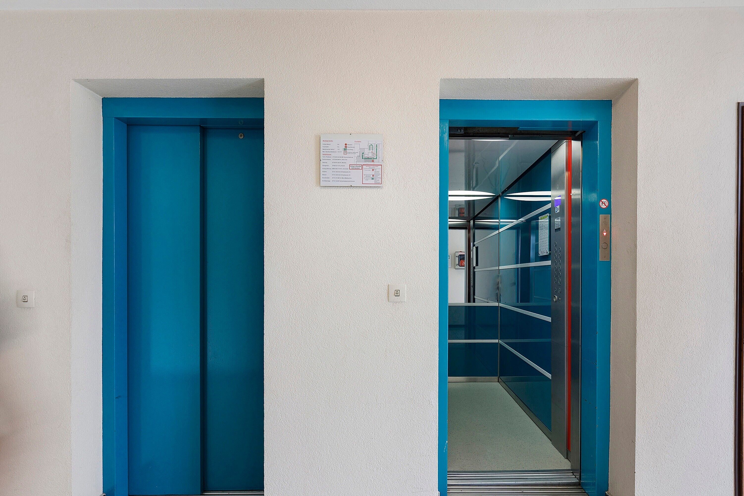 Een gang met twee blauwe deuren, waarvan er een naar een lift leidt.