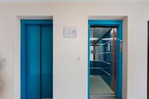 Een gang met twee blauwe deuren, waarvan er een naar een lift leidt.