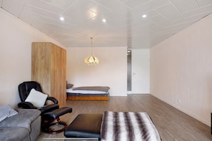 A modern room with a bed, a wooden wardrobe, a leather chair, a bench, and a hanging light fixture.