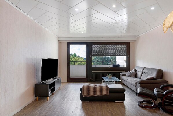 A modern living room with a flat-screen TV, a sofa, a coffee table, and a window with blinds.