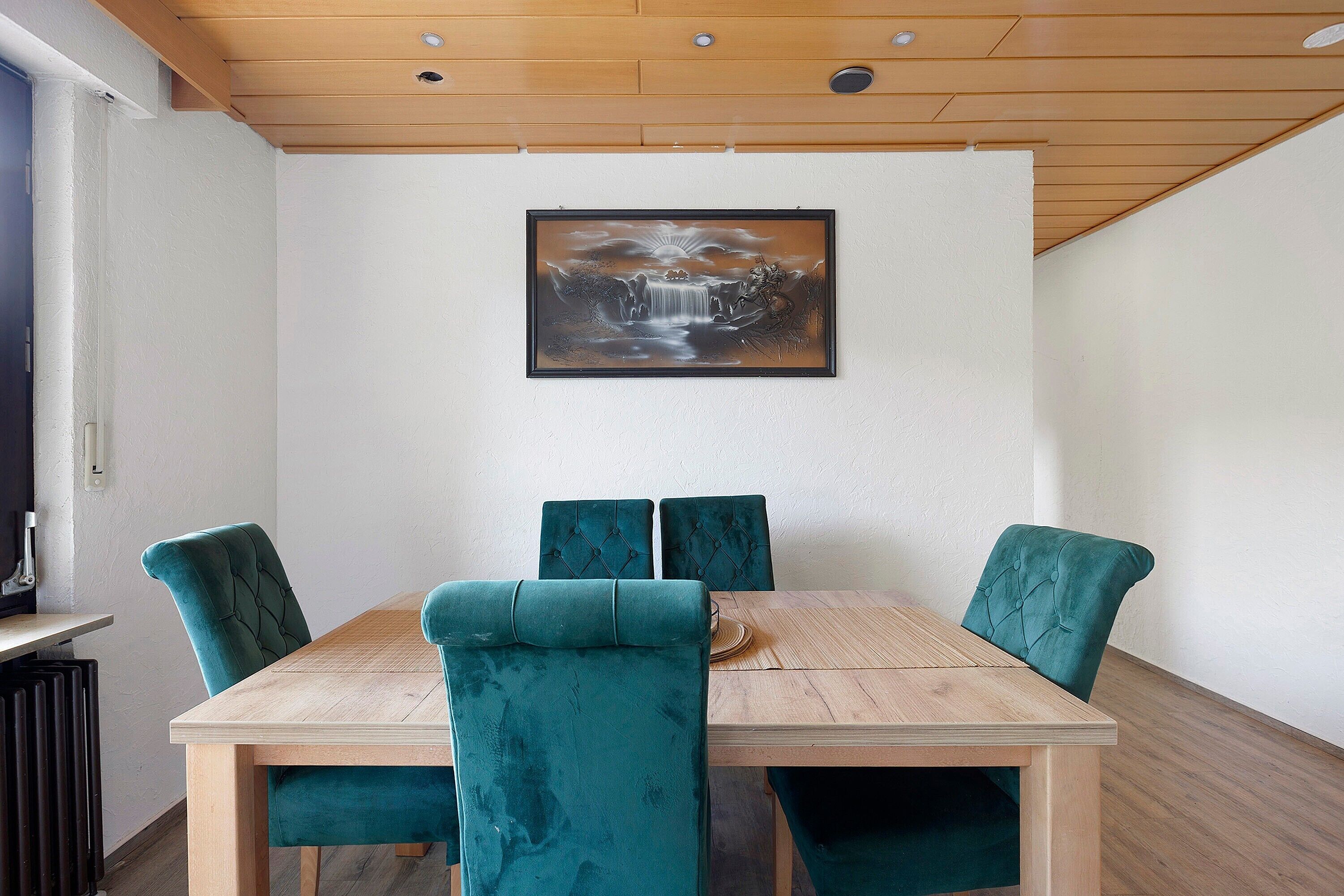A dining area with a wooden table and four teal upholstered chairs.