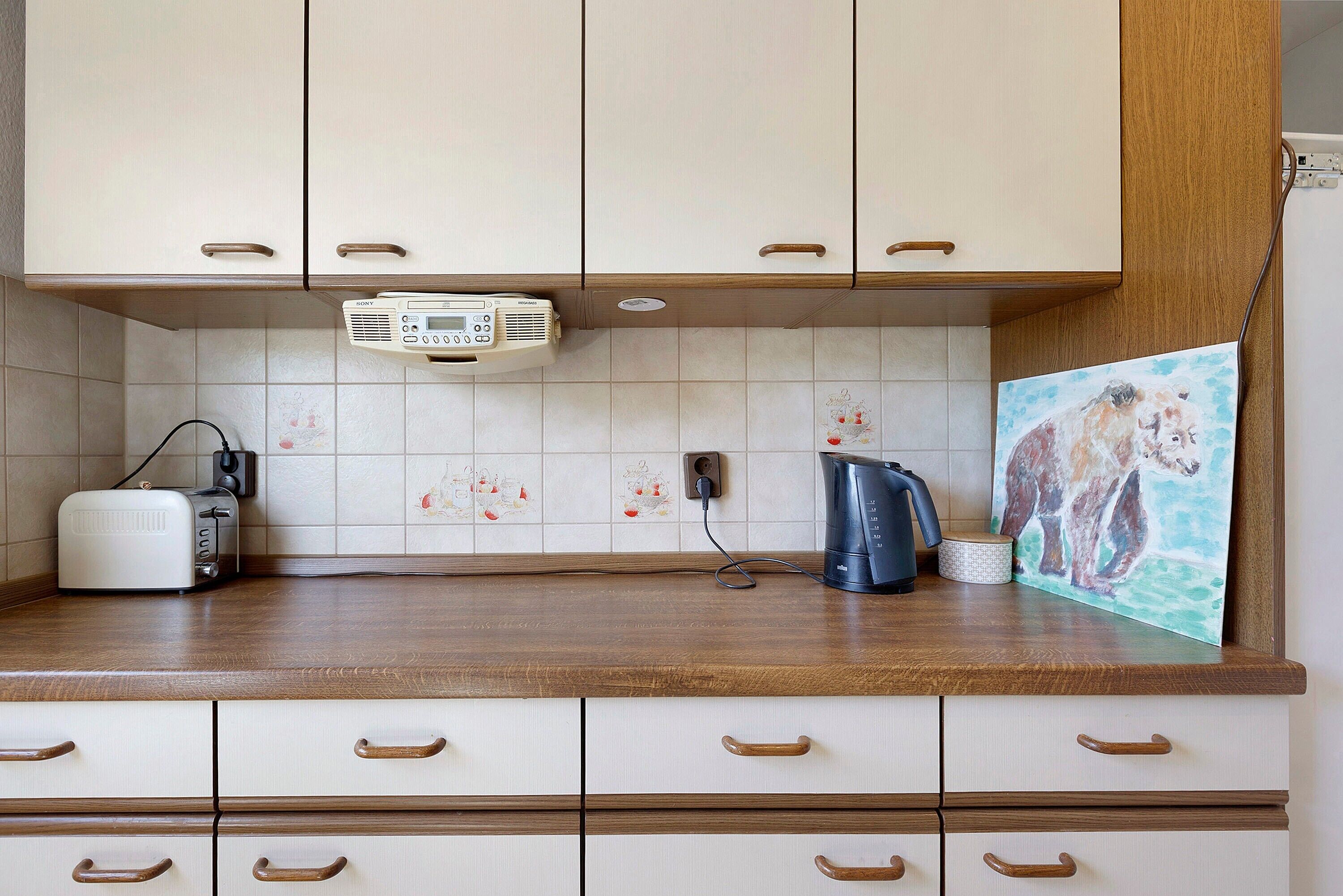 Eine Küche mit weißen Schränken, einem Toaster, einem Wasserkocher und einem Bild an der Wand.