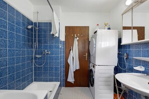 A bathroom with a bathtub, a shower, a sink, and a door with a towel hanging on it.