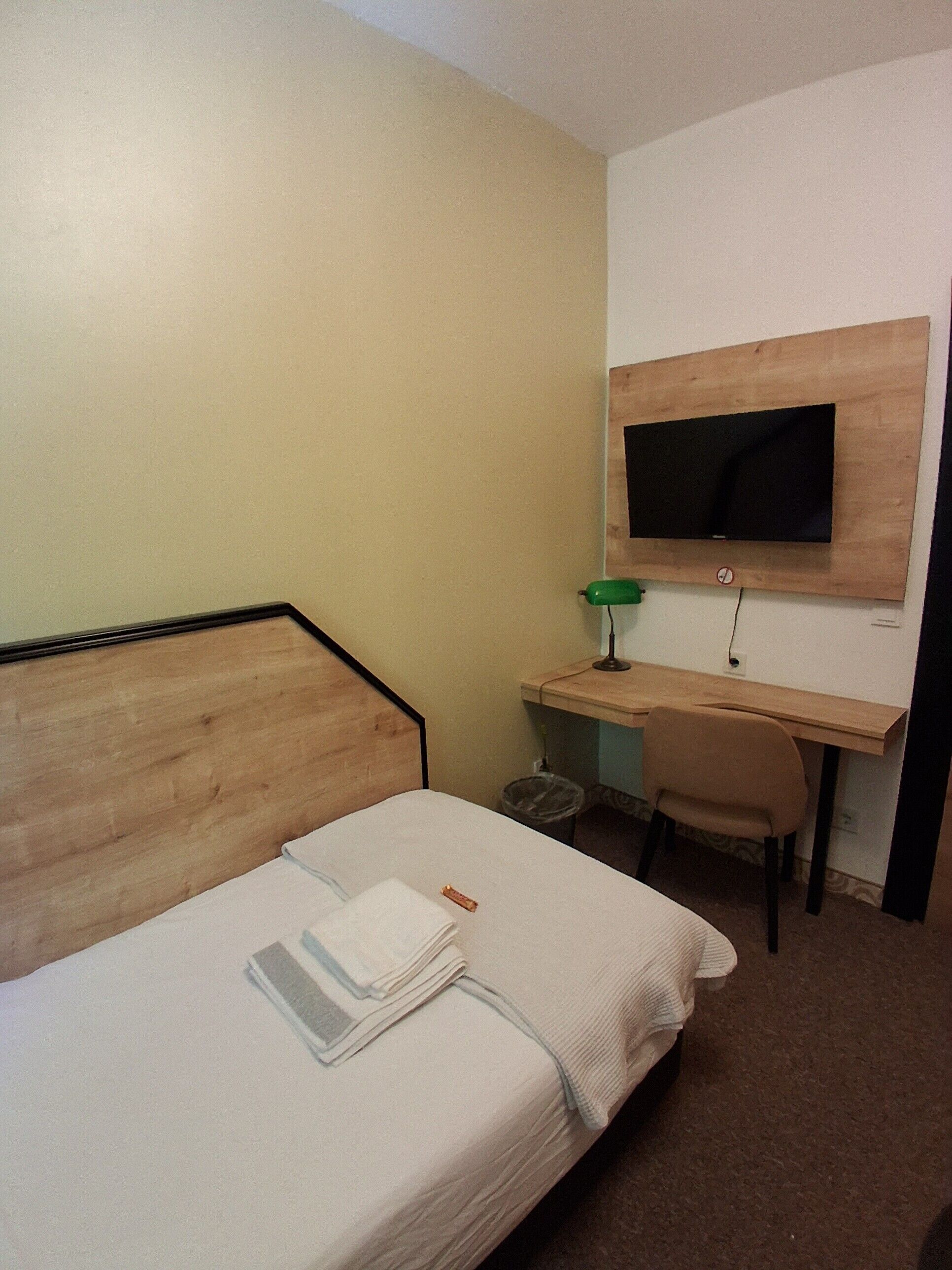 Ein Hotelzimmer mit einem Bett, einem Schreibtisch mit Stuhl, einem an der Wand befestigten Fernseher und einem Mülleimer.