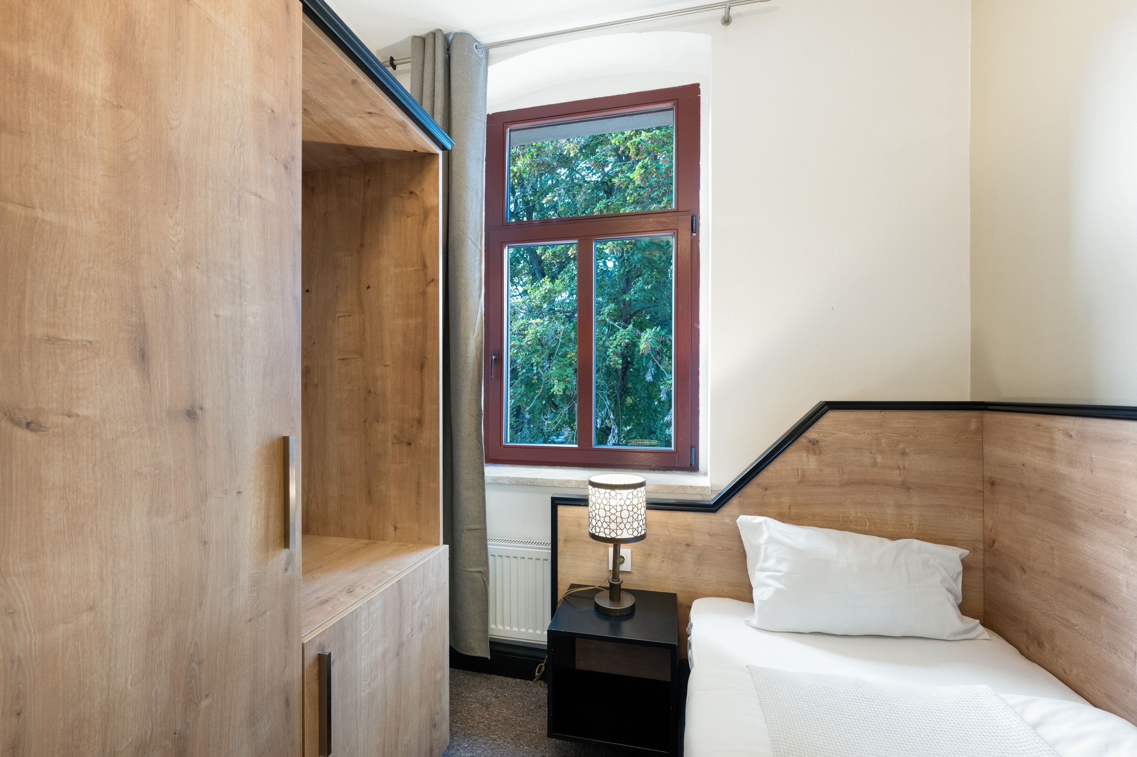 Quarto com cabeceira de madeira, janela com vista para árvores, luminária de cabeceira e cama com roupa de cama branca.