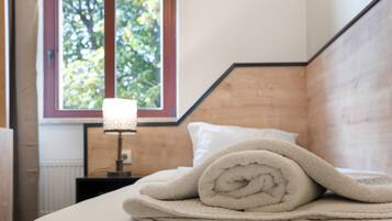 A neatly made bed with a rolled towel, a bedside lamp, and a window with a view of trees.