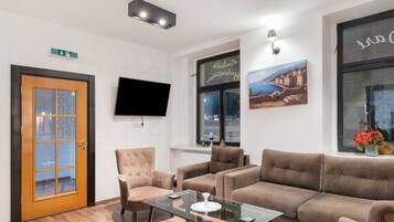 A modern lobby with a wooden door, seating area, flat-screen TV, artwork, and a window with a view.