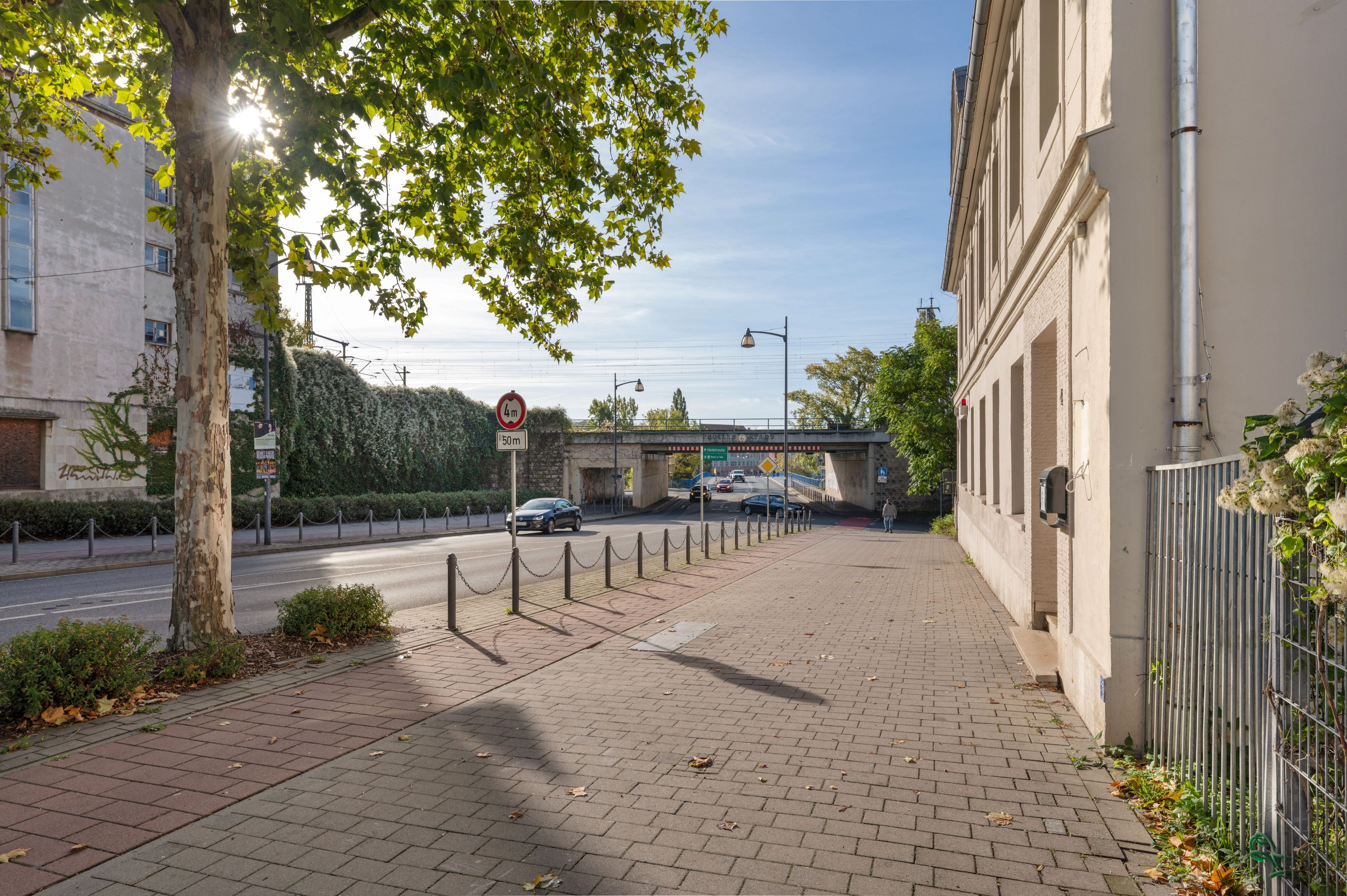 Ein gepflasterter Fußweg, der von einem Metallzaun und einem Gebäude gesäumt wird.