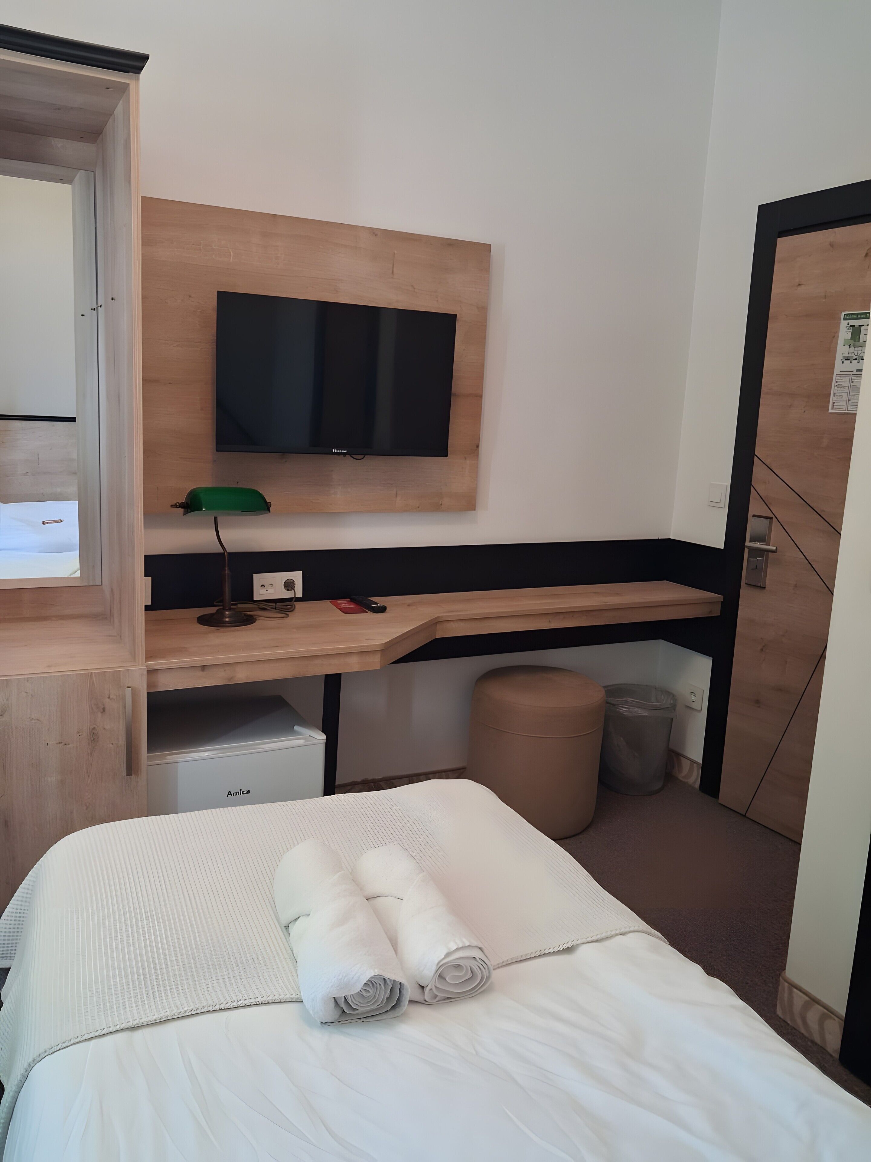 Ein Hotelzimmer mit Bett, Schreibtisch, Flachbildfernseher, Mülleimer und Stauraum.