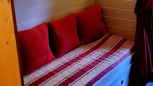 A compact bed with a striped bedspread, red pillows, and a headboard against a wooden wall.