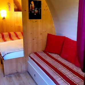 A small, cozy room with two beds, wooden walls, and a sloped ceiling.