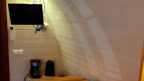 A cozy dining area with a wooden table and chairs, a television mounted on the wall, and a coffee maker on the table.