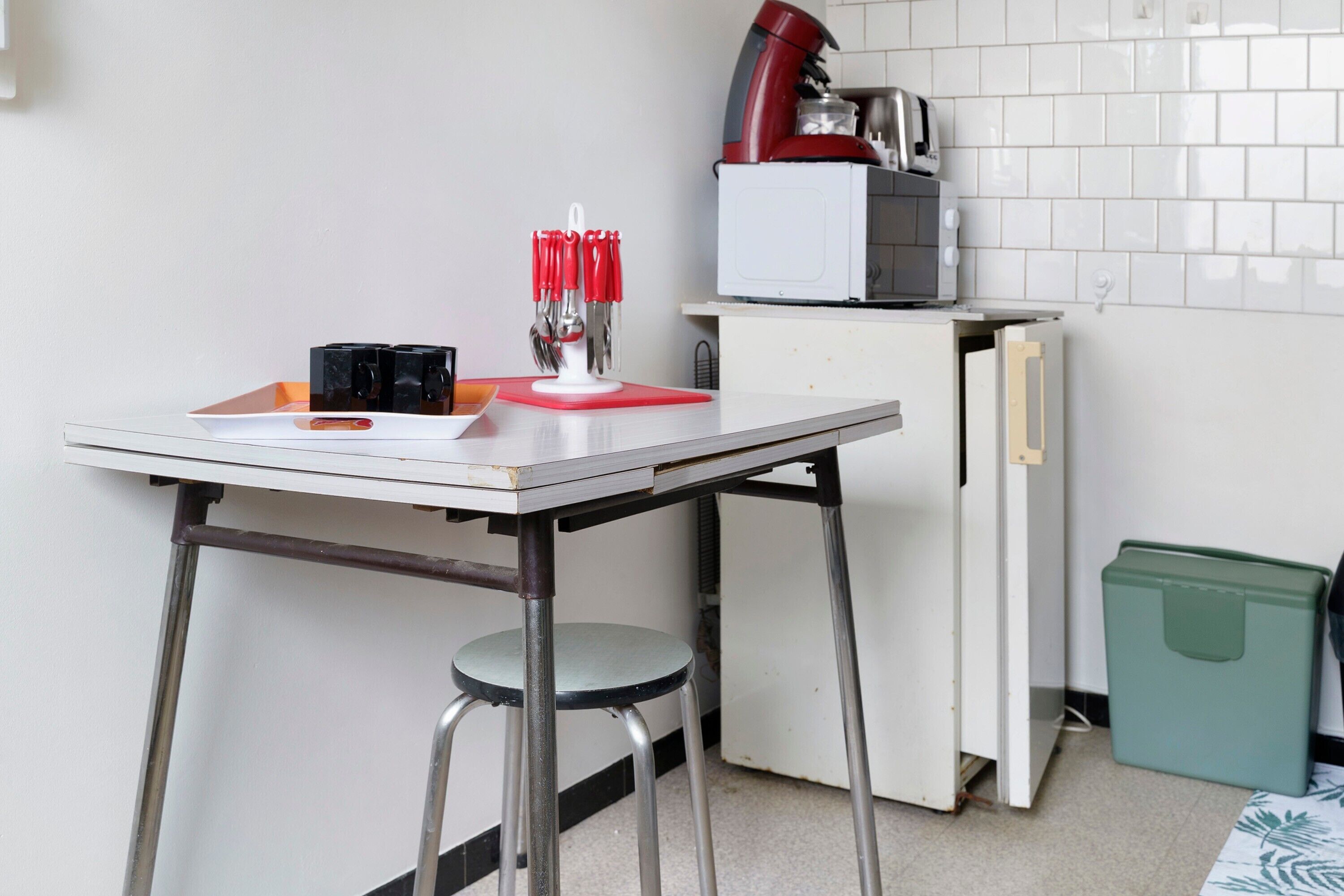 Una piccola cucina con un frigorifero bianco, un forno a microonde, una macchina per il caffè e un tavolo con un portacoltelli.