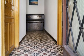 A narrow hallway with patterned floor tiles, a wooden door frame, and a dark wooden cabinet with ornate handles.