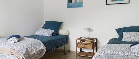 Une chambre avec deux lits, une table de chevet avec une lampe et deux œuvres d’art encadrées au mur.