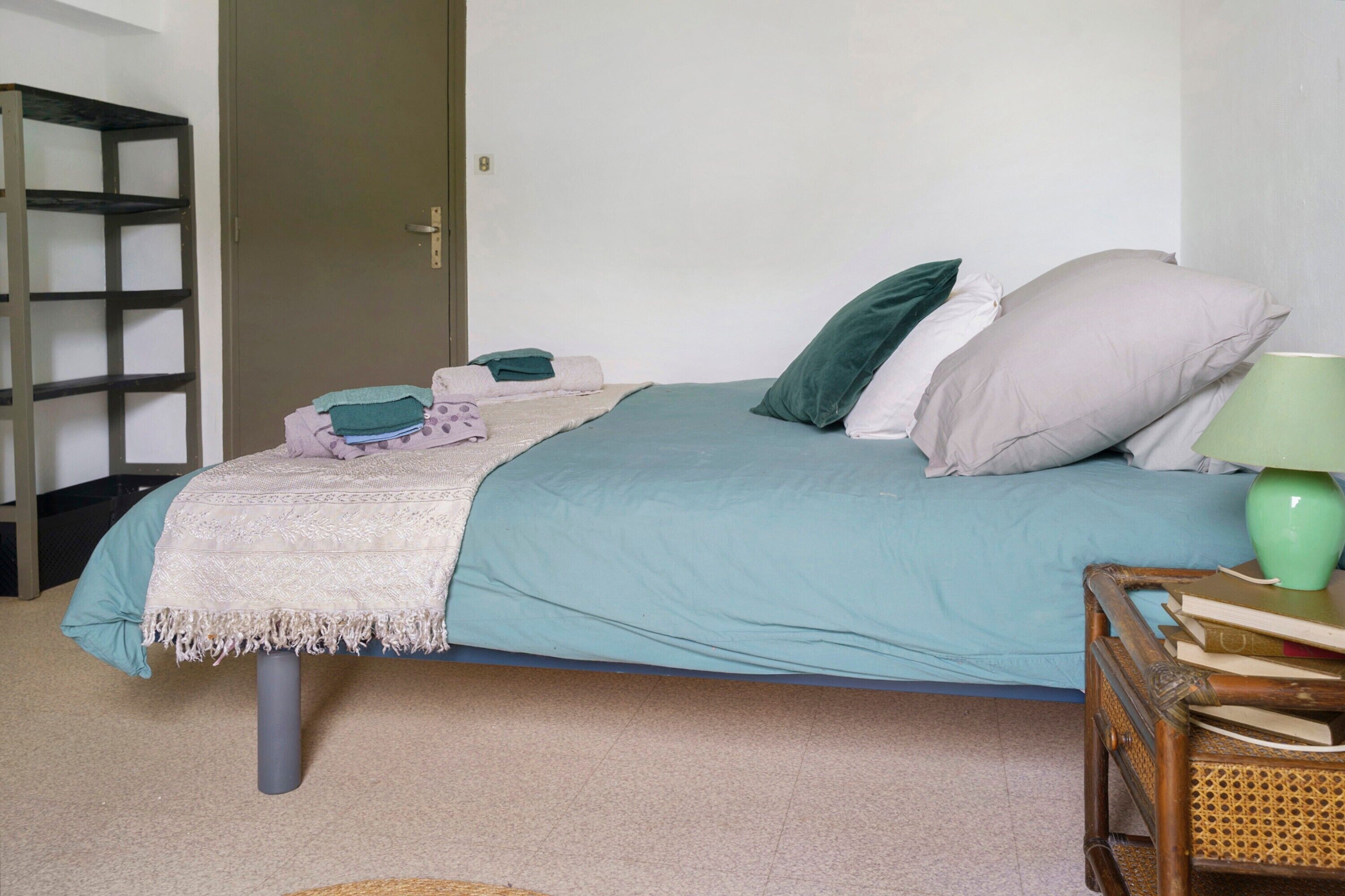 A bedroom with a bed, pillows, a bedside table with a lamp, and a wooden chair.
