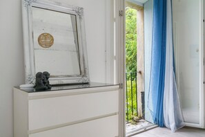 Una habitación con un aparador blanco, un espejo decorativo y vistas a zonas verdes a través de una puerta abierta.