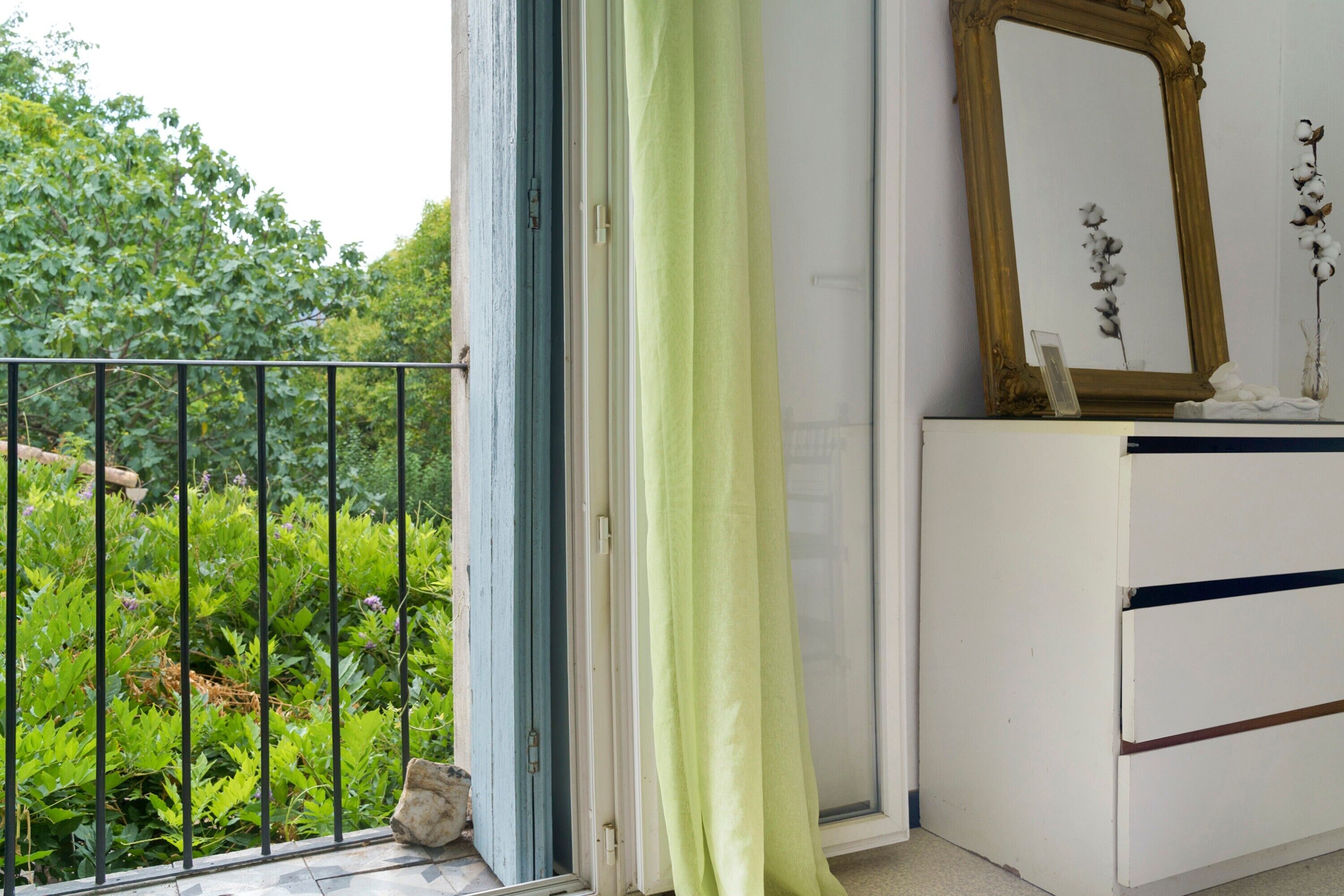A room with a view of greenery outside, a white dresser, a mirror, and a curtain.