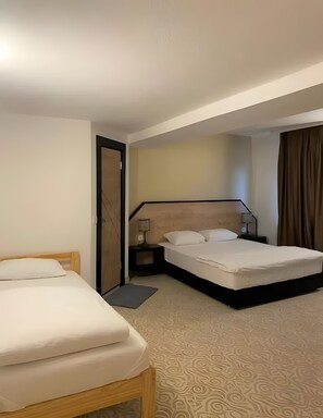 Habitación de hotel con dos camas, una mesita de noche con lámpara, una puerta y una alfombra estampada.