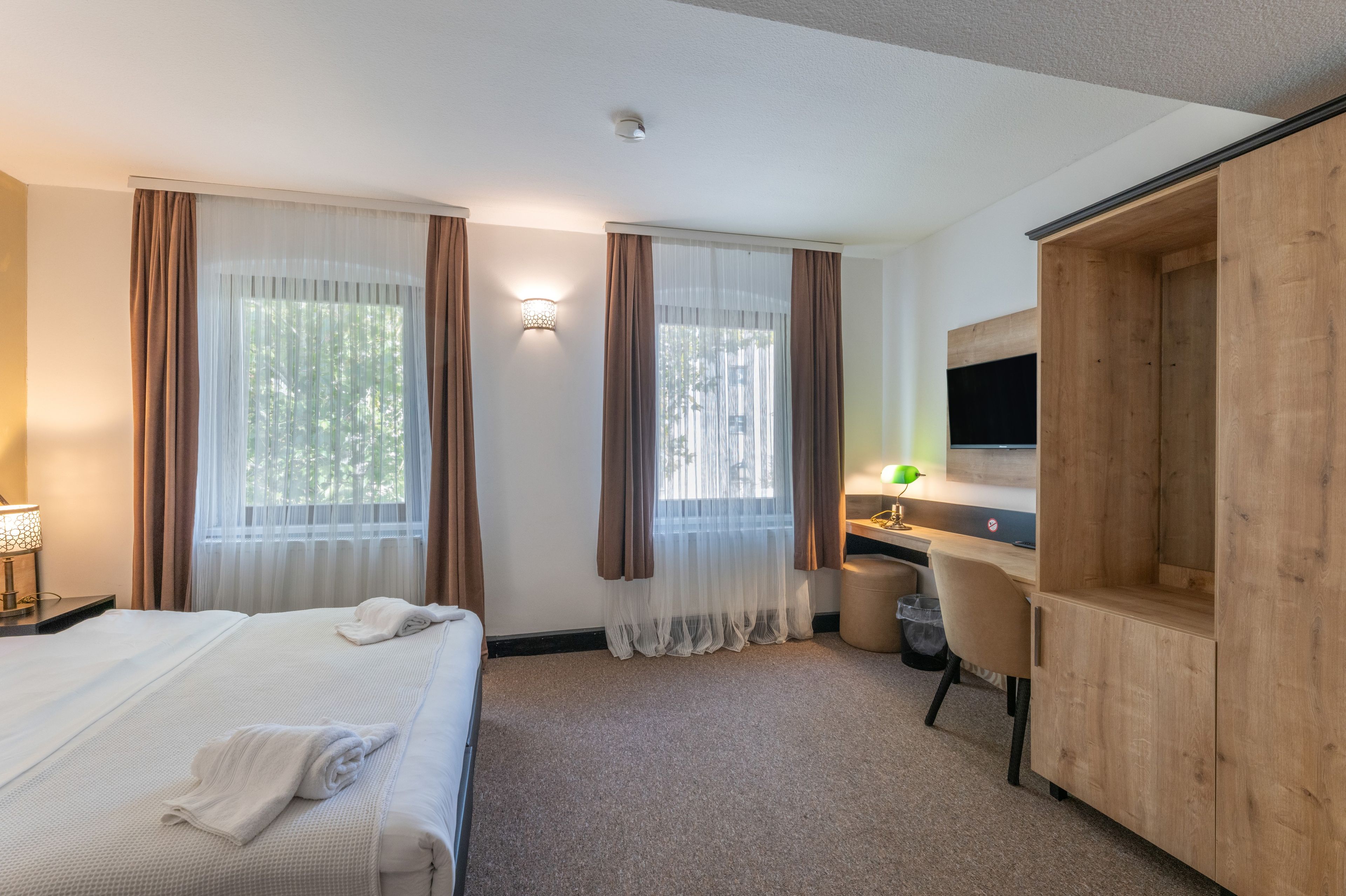 Ein Hotelzimmer mit Bett, Schreibtisch, Stuhl, Fernseher und Kleiderschrank.