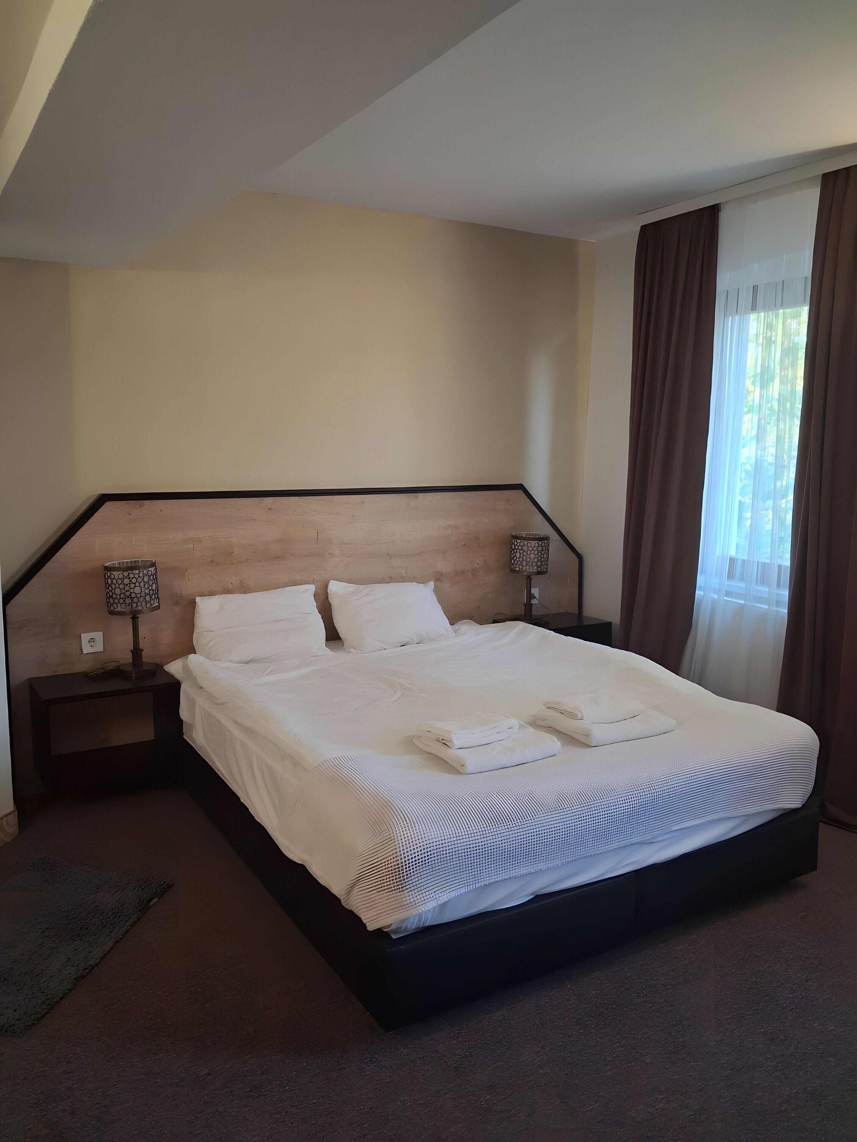 A neatly made bed with white linens and towels, a wooden headboard, and a nightstand with a lamp.
