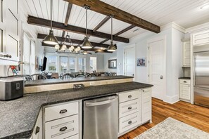 Eine moderne Küche mit Kochinsel, Edelstahlgeräten und einer Deckenverkleidung im Landhausstil.