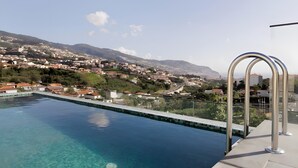 A swimming pool with clear blue water, a metal railing, and a view of a hillside town.