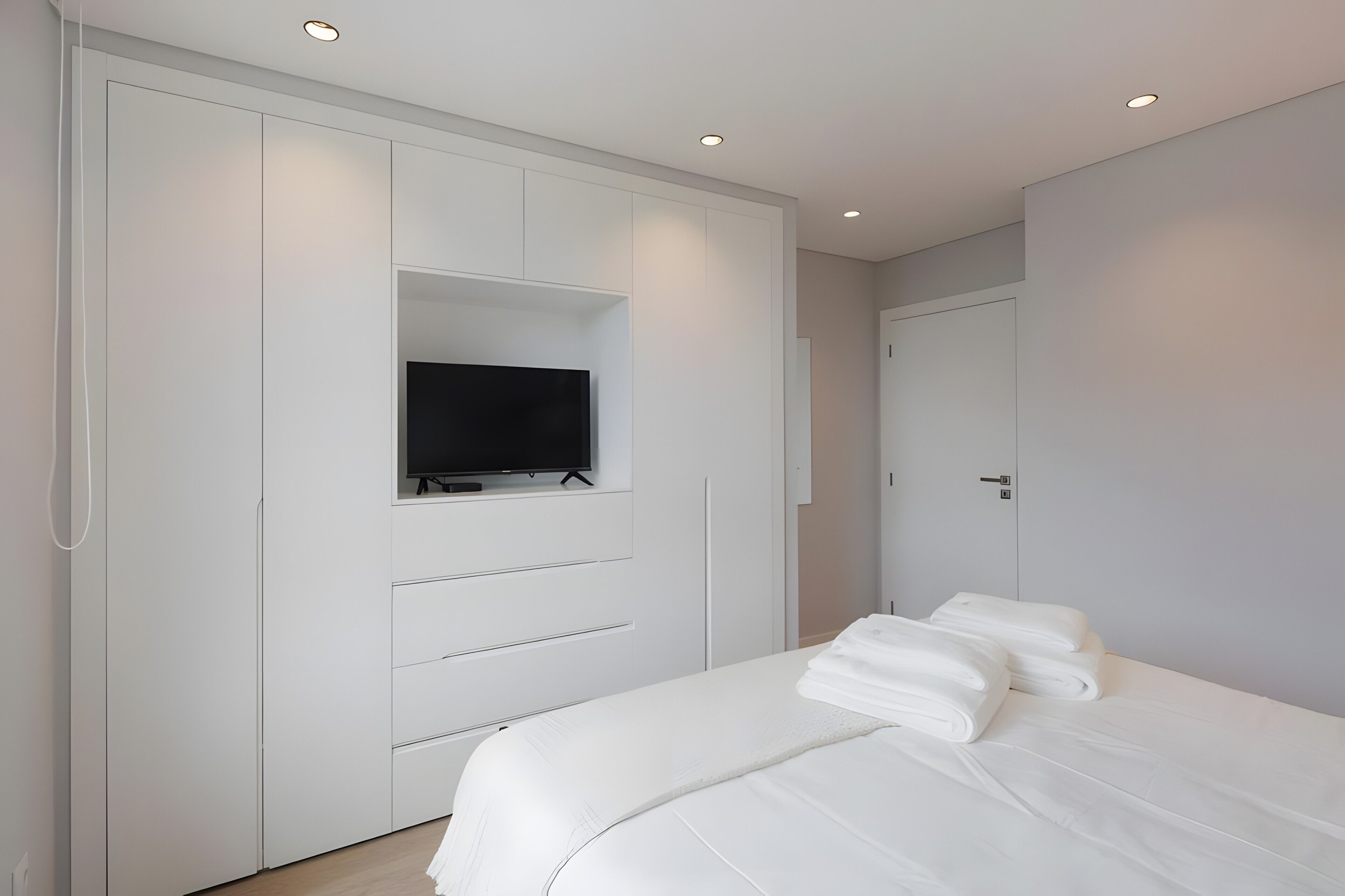 Un dormitorio con una cama, un televisor montado en un armario y una puerta.