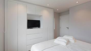 Un dormitorio con una cama, un televisor montado en un armario y una puerta.