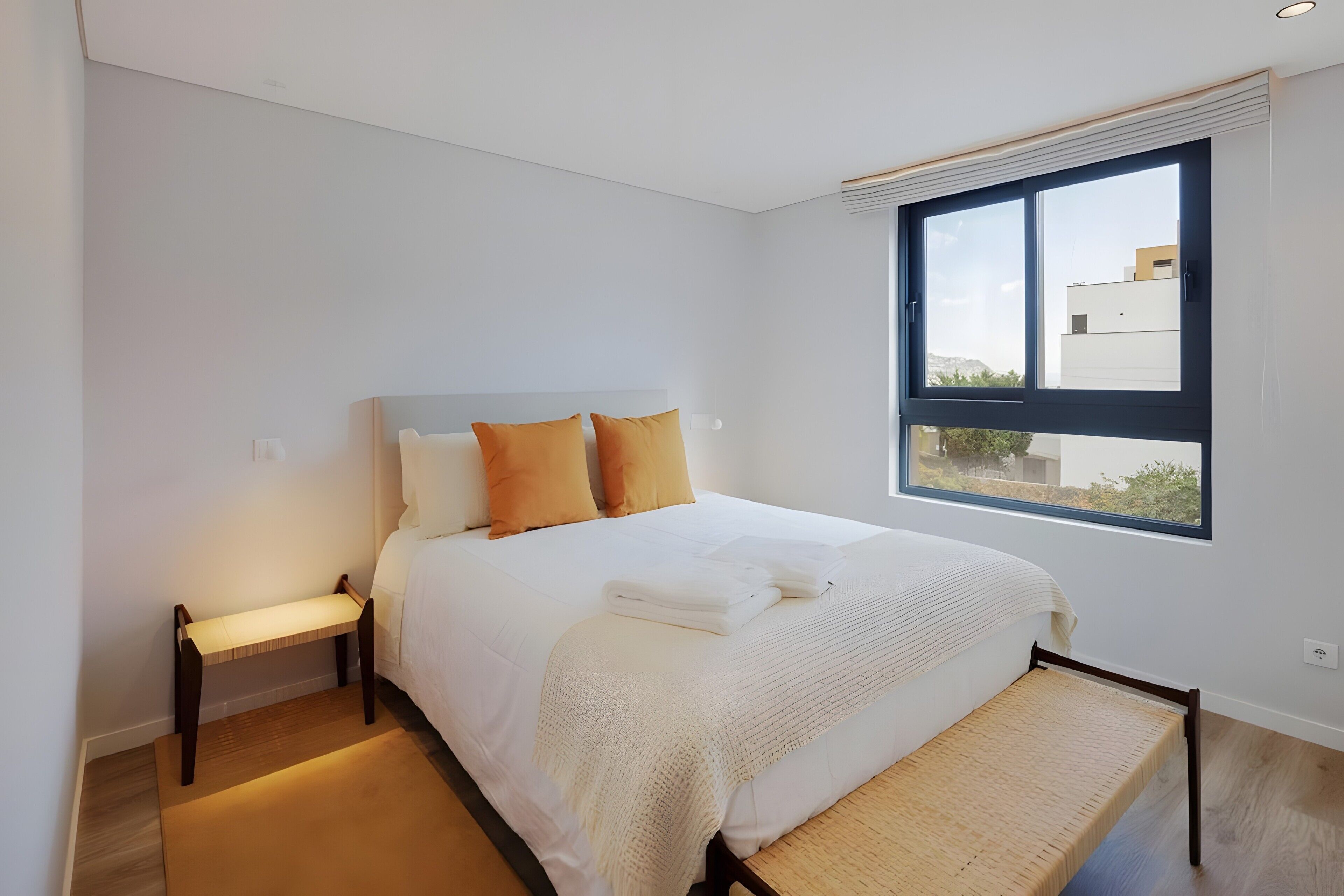 A modern bedroom with a bed, pillows, a bedside table, and a window with a view.