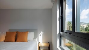 A modern hotel room with a large bed, a small table, and a window with a city view.