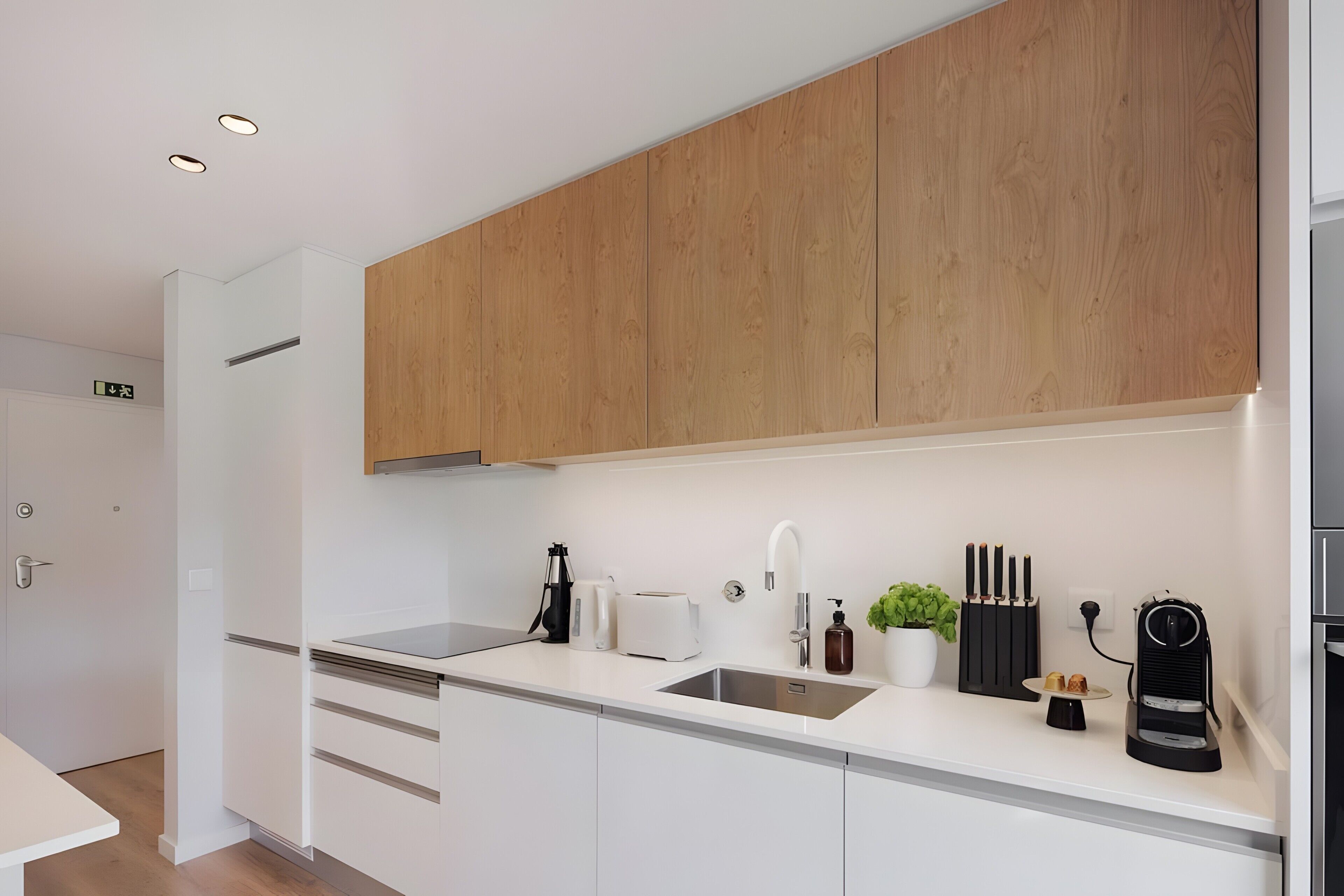 Una cocina moderna con armarios blancos, un estante superior de madera, un lavamanos integrado y varios electrodomésticos, incluyendo una cafetera y un tostador.