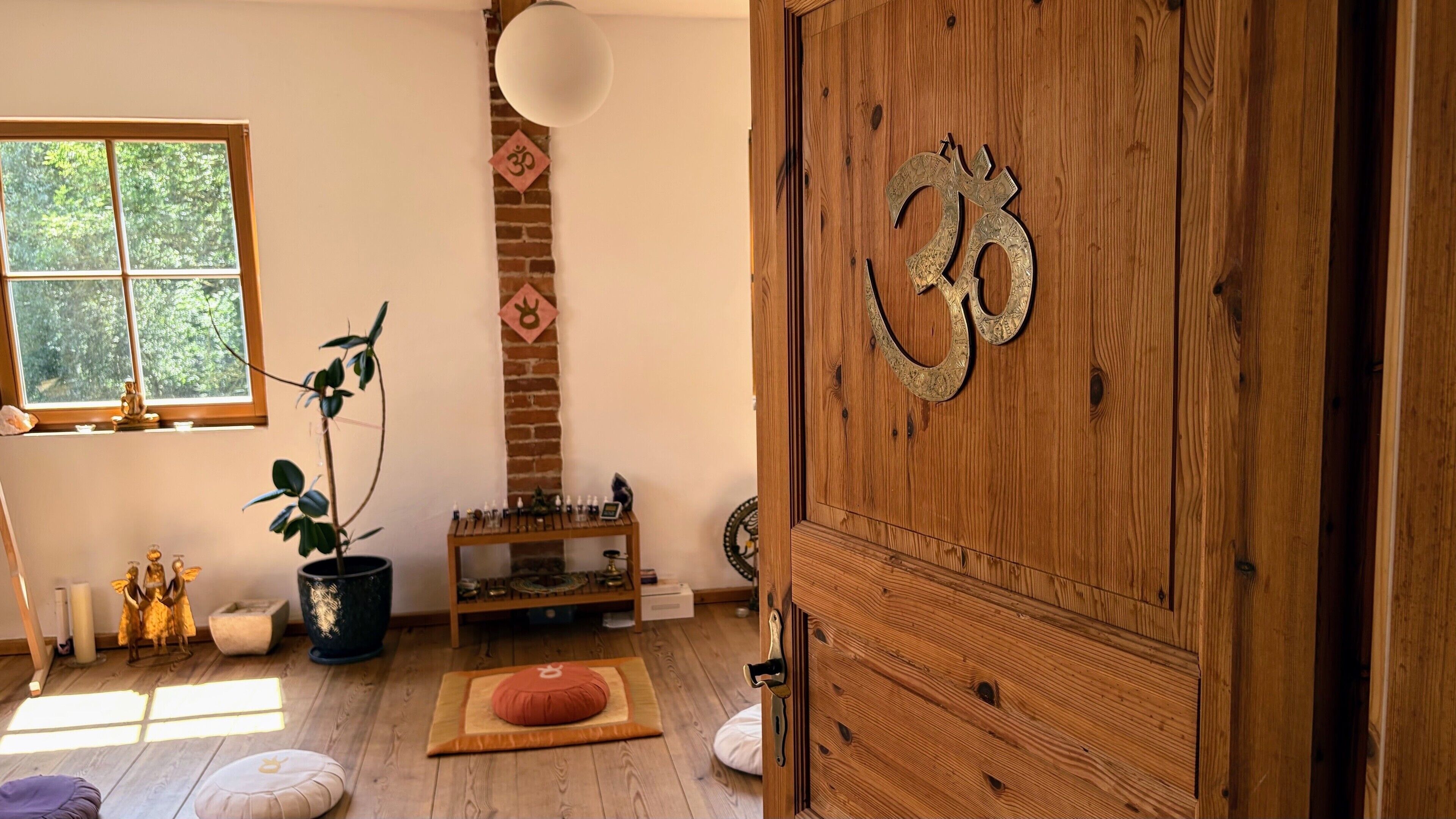 Une pièce dotée d’une porte en bois ornée d’un symbole, d’une cheminée en briques, d’une fenêtre donnant sur des arbres et d’une petite table sur laquelle sont disposés des objets décoratifs.