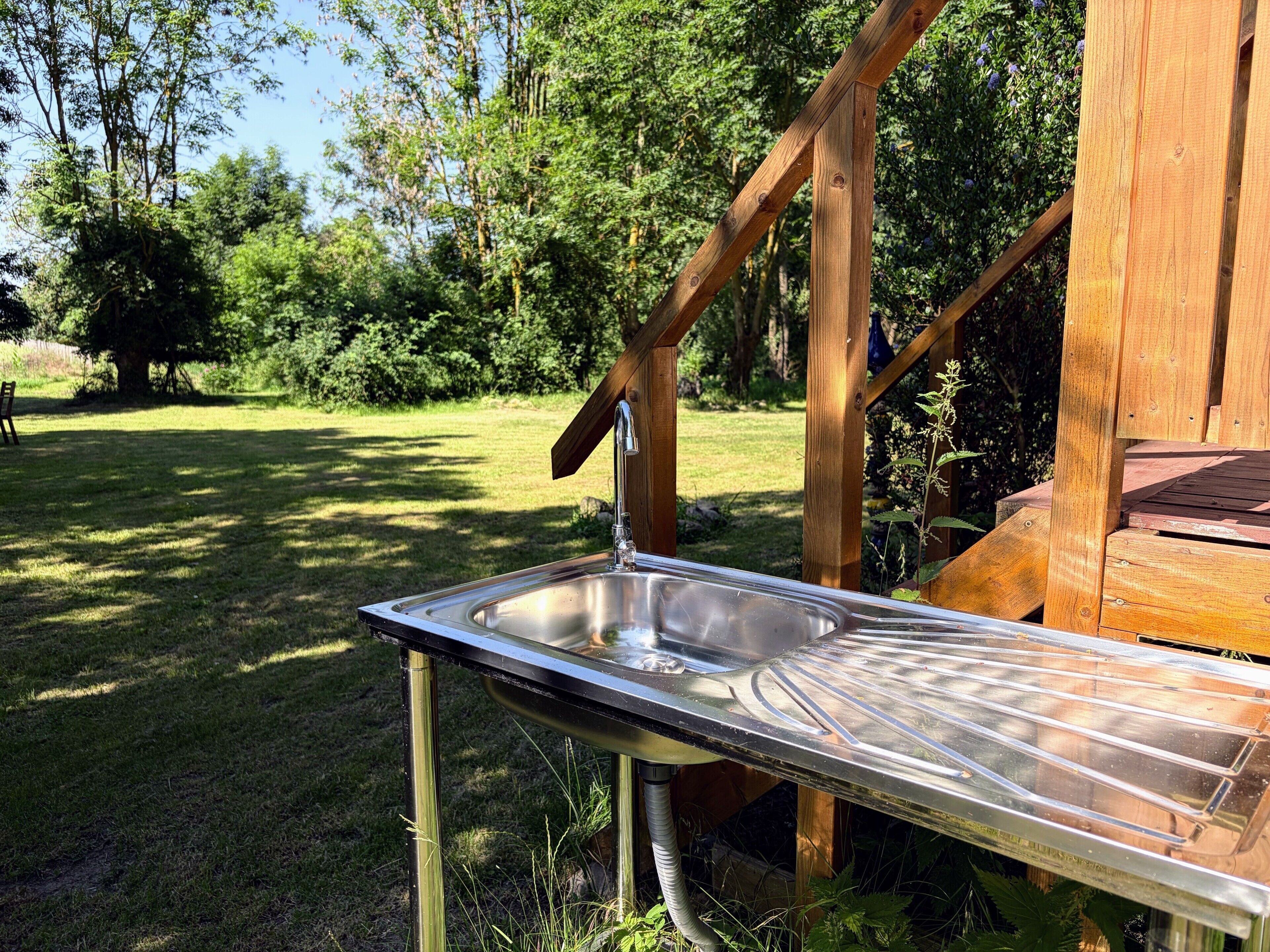 Un lavamanos de acero inoxidable al aire libre, con una estructura de madera al fondo.