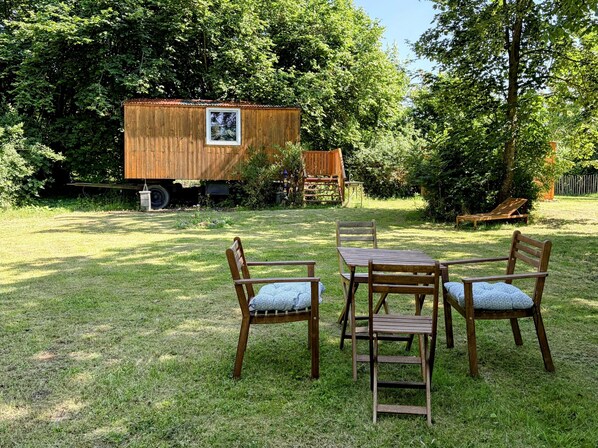 A wooden deck with a table and chairs, surrounded by lush greenery and a wooden structure in the background.